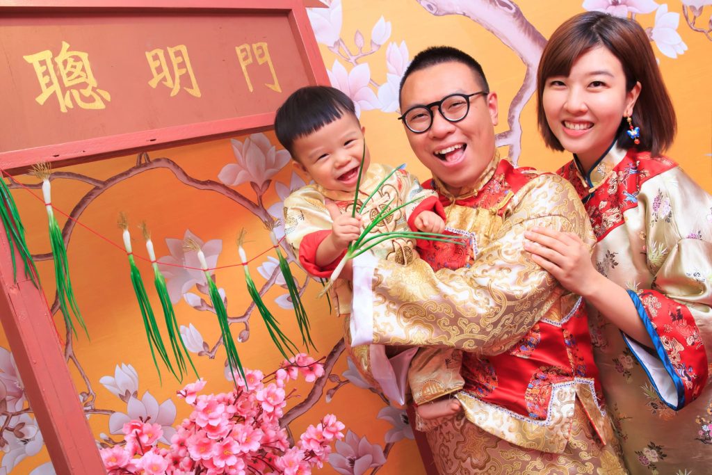 寶寶穿著中式抓周服飾開心摸蔥門，象徵智慧與好兆頭的抓周儀式場景