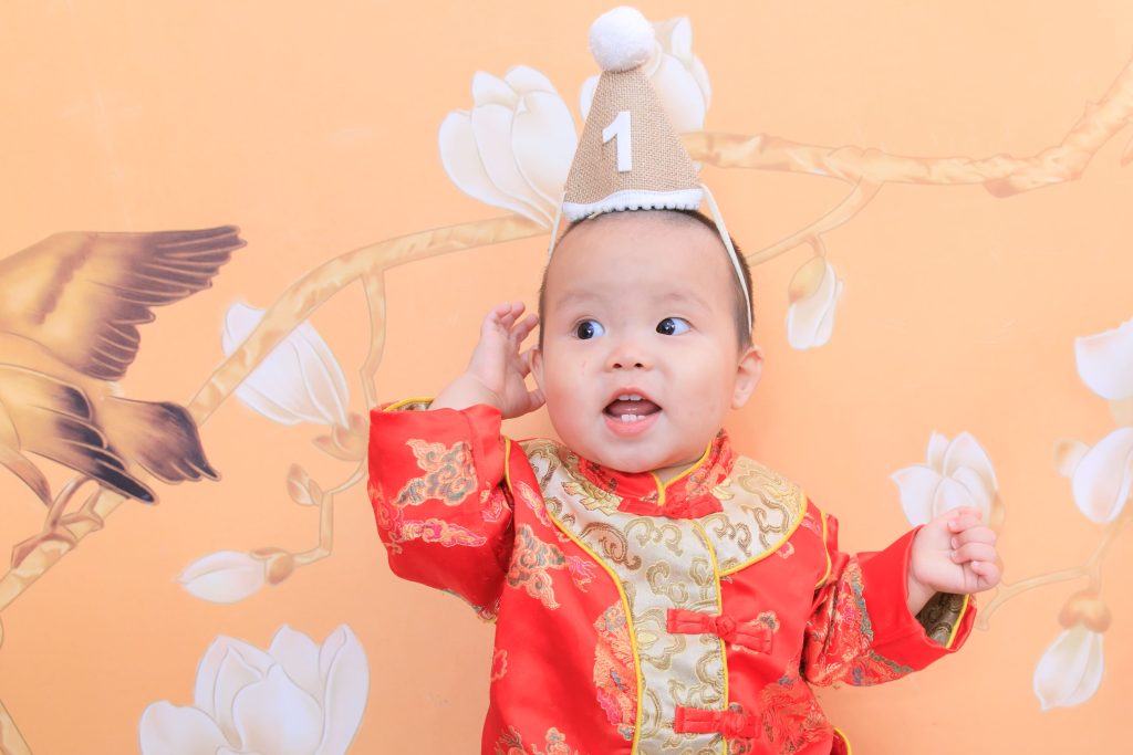 寶寶一歲抓周紀念，小男嬰穿紅色中式服裝戴生日帽，呈現喜氣溫馨畫面